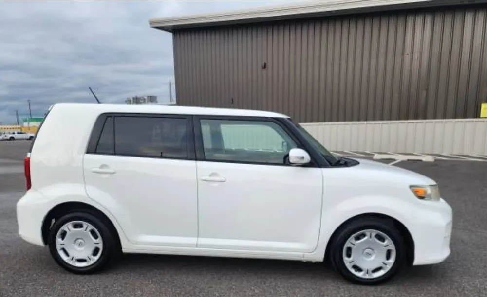 Side view of a clean white Scion xB parked outside a metal building